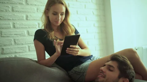 Woman using her tablet, man his laptop at home Stock Footage 68802094