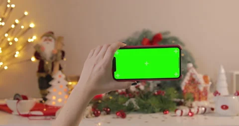 A woman using an iPhone 12 with a green screen on a Christmas background. Video stock 144354848