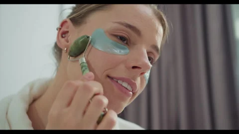 A woman using a jade roller on her face to improve her skin care routine Stock Footage 274100986