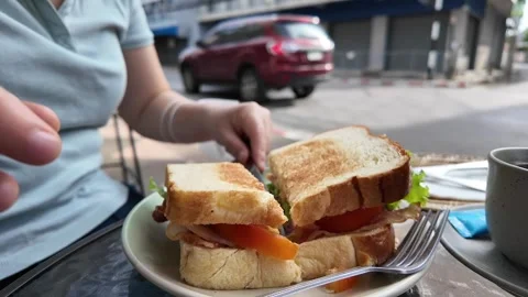 Woman using knife and fork cutting classic club sandwiches in half at cafe. Vidéo 277557371