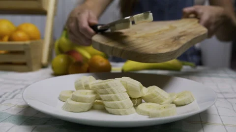 Woman using knife to scrape banana pieces onto plate - closeup, slow motion shot Stock Footage 341207367