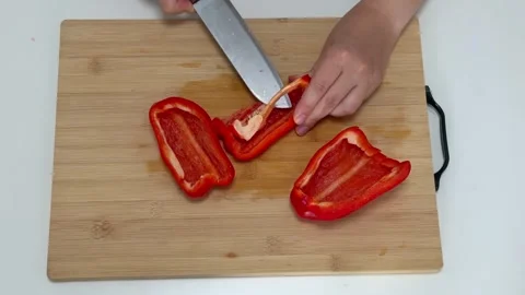 Woman using knife to slice red bell pepper on wooden cutting board for meal Stock Footage 319421258