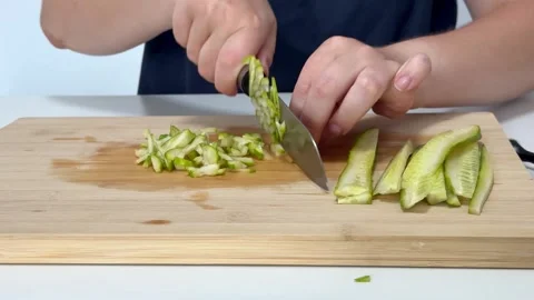 Woman using knife to thinly slice cucumber on cutting board in kitchen Stock Footage 318645152