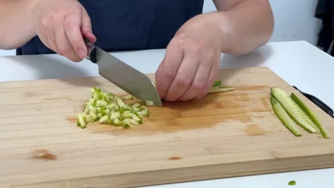 Woman using knife to thinly slice cucumber on cutting board in kitchen Video stock 319421293
