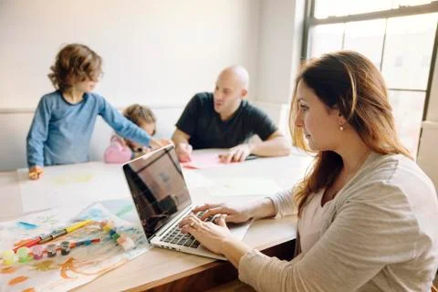 Woman using laptop computer while father assisting children in drawing at table Stock Photos