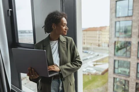A woman is using a laptop computer while looking out of a window Stock Photos