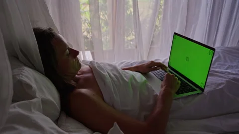 Woman Using Laptop with Green Screen While Resting in Bed Near Window and Soft C Stock Footage 336694557
