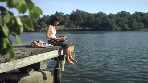 A woman using a laptop on a jetty by a lake Stock Footage 11287853