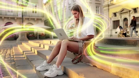A woman is using a laptop surrounded by vibrant digital light trails in an urban Stock Footage 277420016