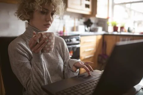 Woman using laptop while having coffee at home 写真素材