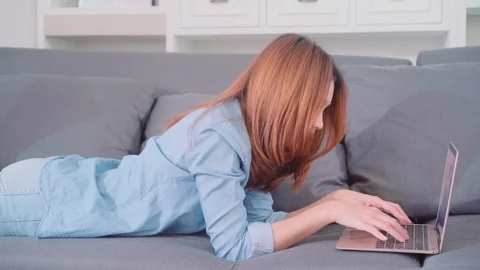 Woman using laptop while lying on sofa at home. Stock Footage 97501134