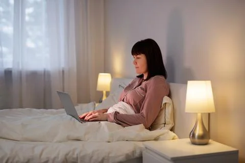 Woman using laptop while lying in her bed Stock Photos