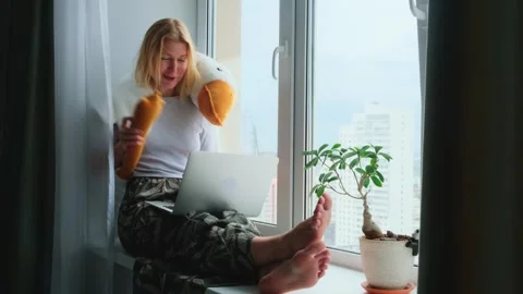 Woman using a laptop while sitting on a windowsill with a funny plush toy. Stock-Footage 253138761