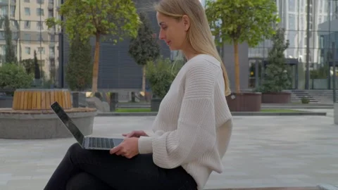 Woman using laptop while sitting outdoors near IT Park buildings in Tashkent Stock Footage 318387766