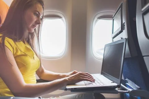 Woman using laptop while is sitting in plane near window Stock Photos