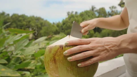 Woman Using Large Knife to Cut into Green Coconut Placed on Balcony Edge Stock Footage 316167727