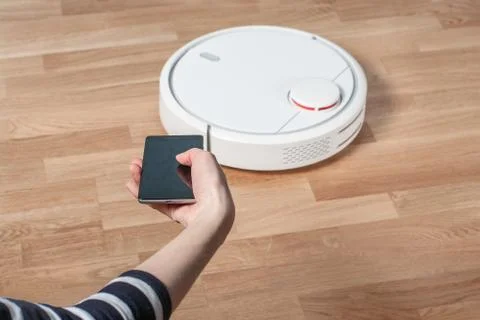 Woman using mobile to control robotic vacuum cleaner Stock Photos