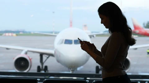Woman using mobile device, half length silhouette against blurred airliner Video stock 86482793