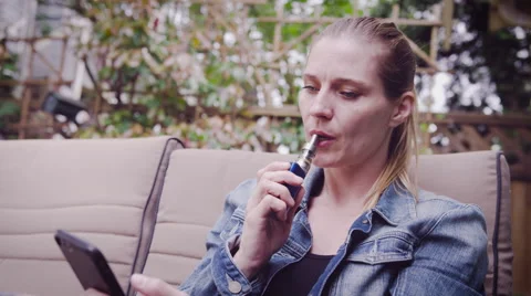Woman using mobile phone while vaping electronic cigarette Stock Footage 64454523