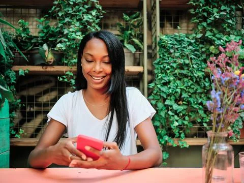Woman using a mobile phone while sitting in a restaurant or coffee shop garden. Stock Photos