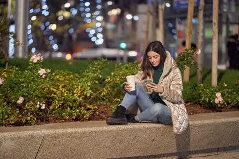 Woman using mobile phone while sitting outdoors with coffee cup. Fotos de archivo