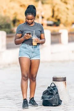 Woman using a mobile while drinking a shake with a bag next to her outdoors Stock Photos