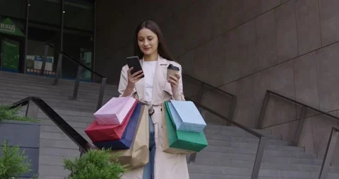Woman using mobile while standing with bags near mall Stock Footage 162075405