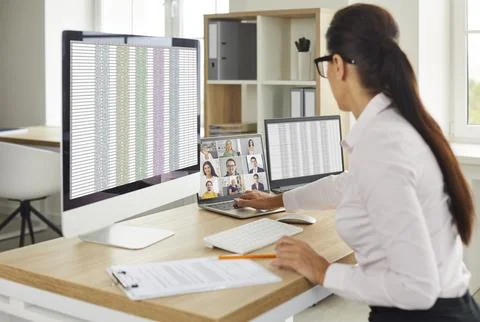 Woman using multiple office computers, working with spreadsheets and having a Stock Photos