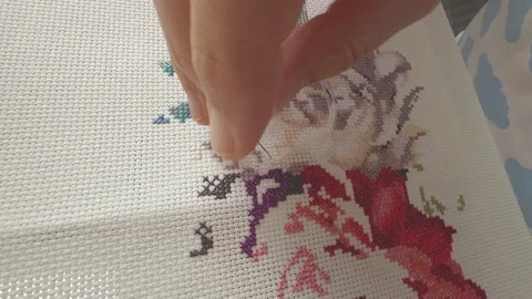 A woman using a needle and thread to create a cross-stitch embroidery pattern Stock Footage 335510780