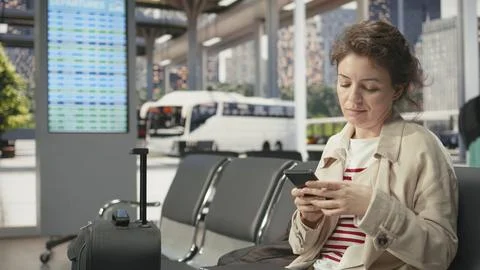 Woman using notebook in bus terminal while listening to music in earbuds Stock Photos