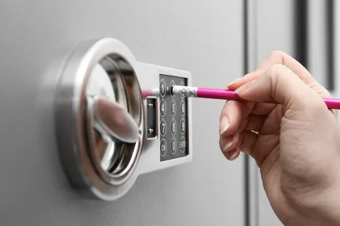Woman using pencil to enter code on keypad of modern safe, closeup Stock Photos