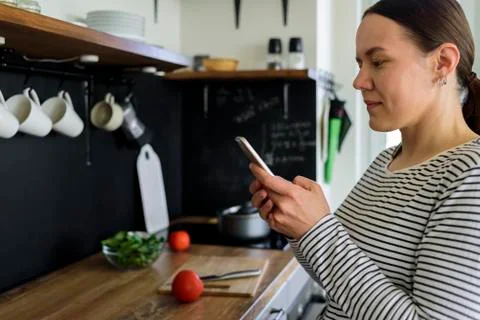 Woman using phone while cooking Stock Photos