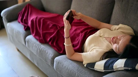 Woman using phone while lying down on sofa Stock Footage 146770352