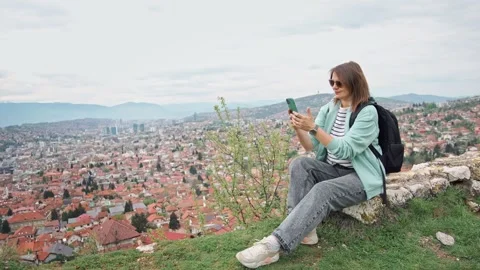 A woman using a phone while sitting on the hill with a beautiful top view  Stock Footage 240707292