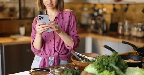 Woman using phone while standing with healthy food in the kitchen at home Stock Footage 172447554