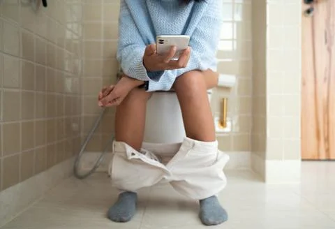 Woman using phone while using the bathroom Stock Photos