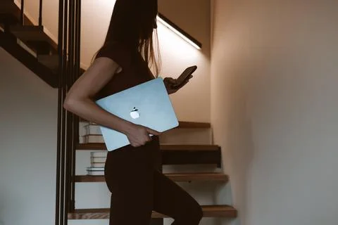 Woman using phone while walking up stairs with Apple MacBook laptop Stock Photos