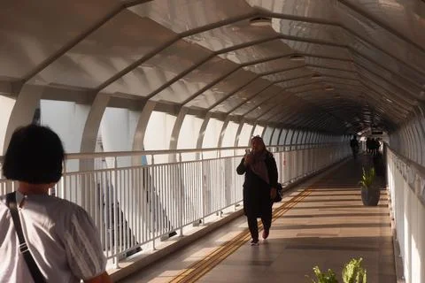 Woman Using Phone While Walking Through Bridge Corridor Stock Photos