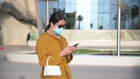 Woman using phone while wearing surgical face mask in an outdoor mall Stock Footage 147291071