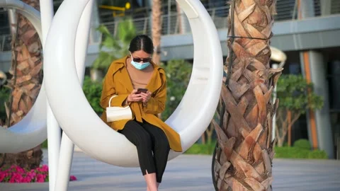 Woman using phone while wearing surgical face mask in an outdoor mall Stock Footage 147291088