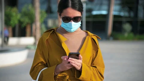 Woman using phone while wearing surgical face mask in an outdoor mall Stock Footage 147291139