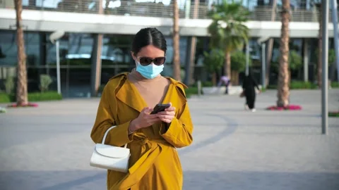 Woman using phone while wearing surgical face mask in an outdoor mall Stock Footage 147291143