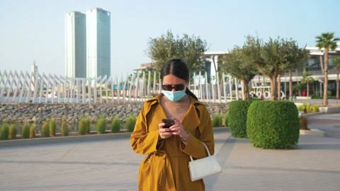 Woman using phone while wearing surgical face mask in an outdoor mall Stock Footage 147291179