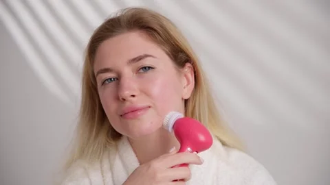 The woman is using a pink device to clean her skin 스톡 동영상 269006003