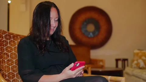 Woman using pink smartphone while sitting on patterned sofa indoors Video stock 341423990