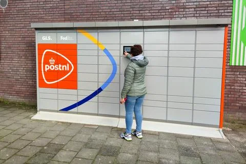 Woman using PostNL parcel locker self-service terminal for delivery pickup 스톡 사진