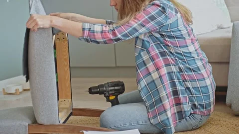 Woman using power drill to attach part during chair assembly Stock Footage 312335186