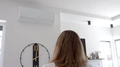 Woman using remote control to adjust temperature on air conditioner Stock Footage 336608178