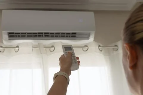 Woman using remote control to adjust temperature on modern white air condit.. Stock Photos