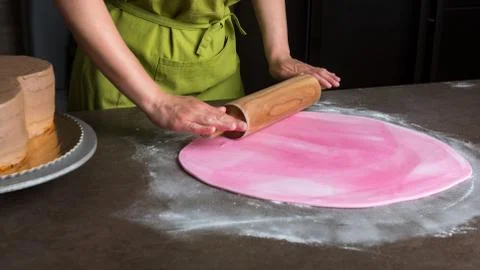Woman using rolling pin preparing pink fondant for cake decorating, hands det Stock Photos